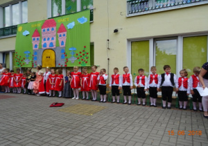 Taras przedszkolny, a na nim scenografia przedstawiająca zamek. Na tarasie stoją przedszkolaki ubrane w stroje odpowiednie do przedstawienia.
